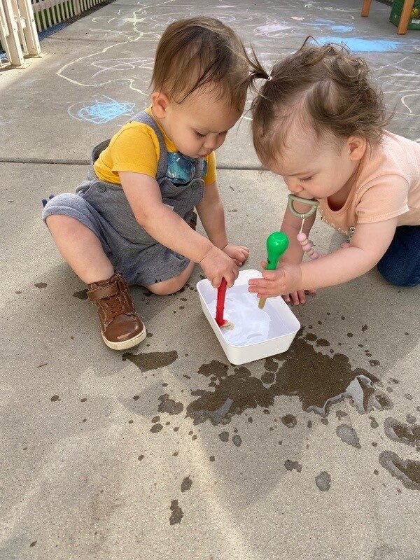 Toddlers pouring water during outdoor play