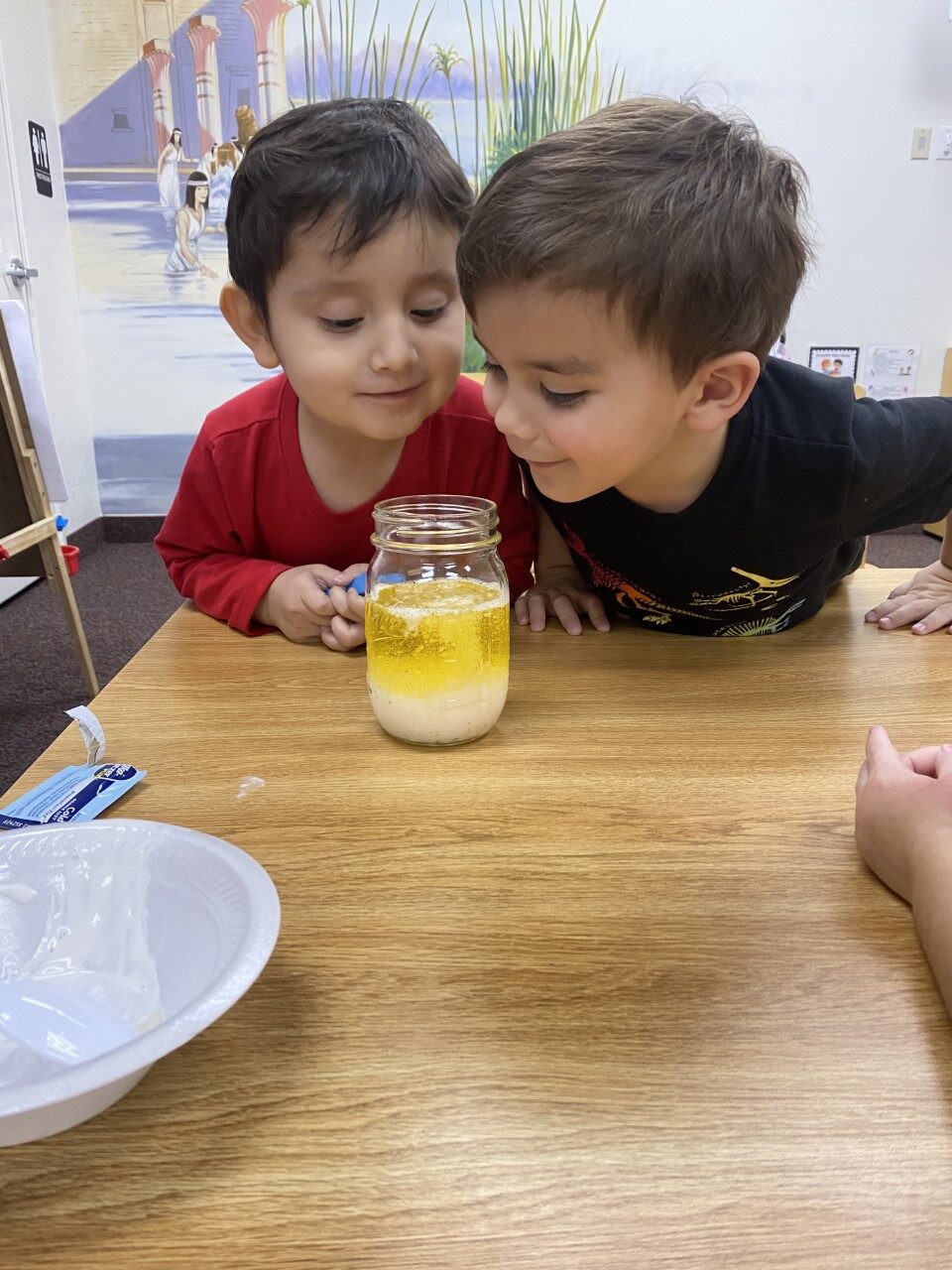 Two children watching a science experiment in a jar