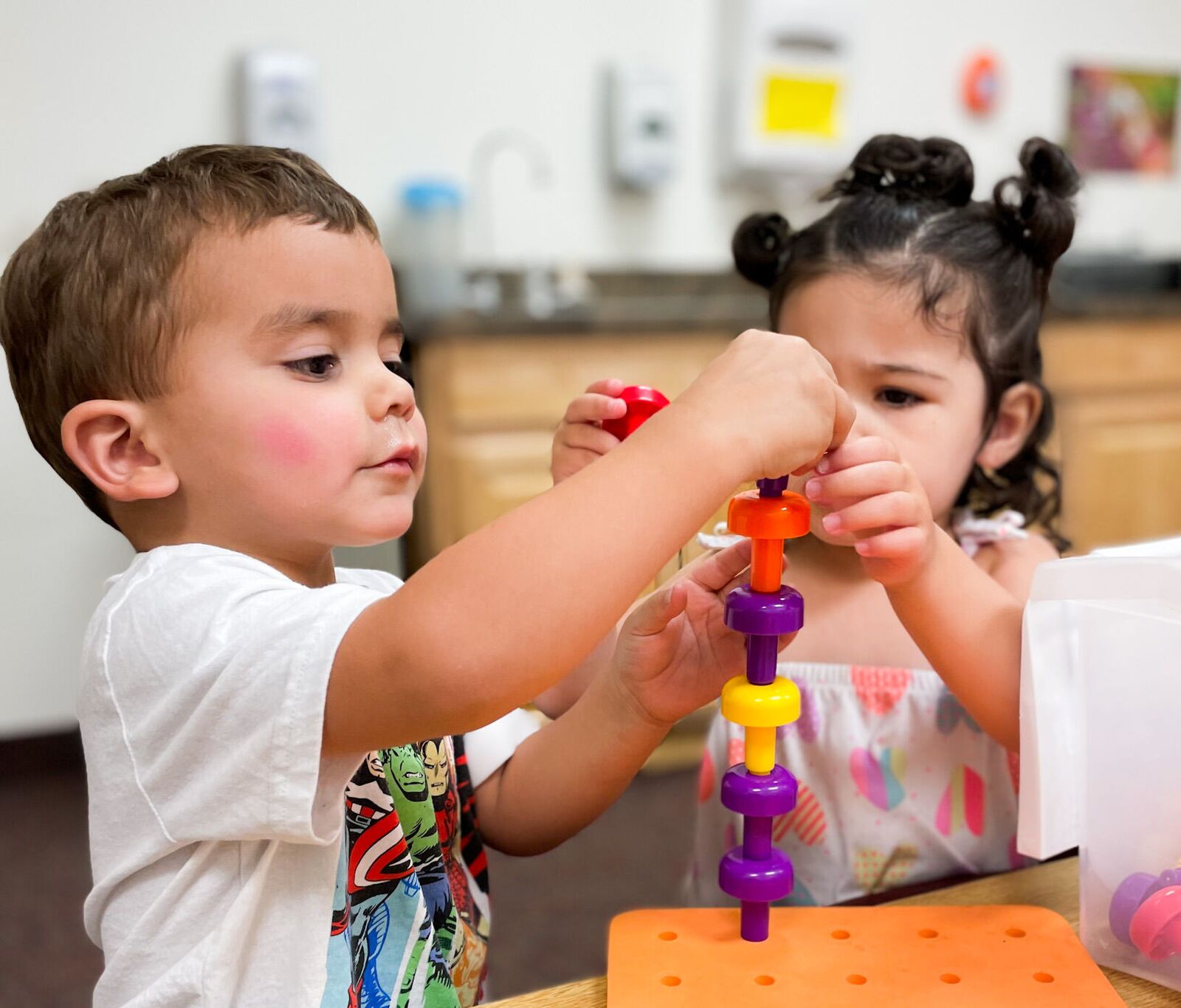Two children building towers with stacking pegs at a table