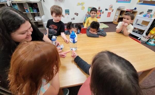 A teacher sitting at a low table with a small group of toddlers