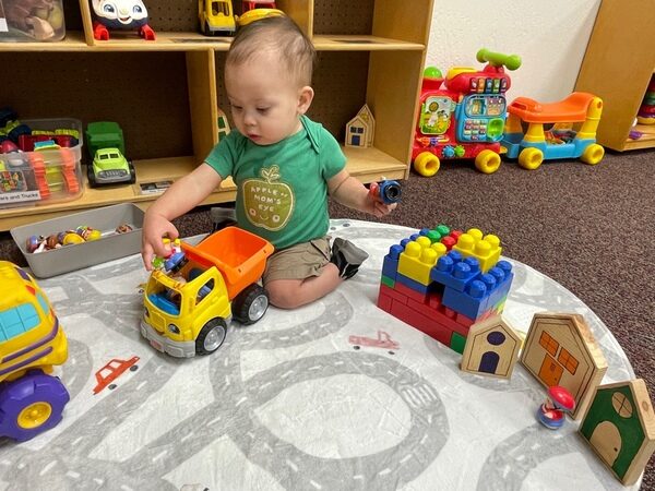 A toddler playing with toy trucks and building blocks
