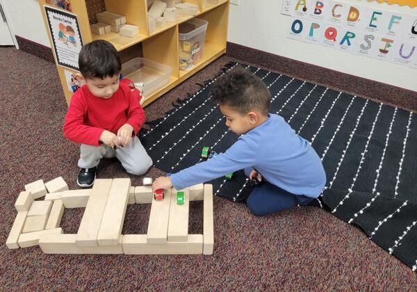 Two children building with wooden blocks on the rug